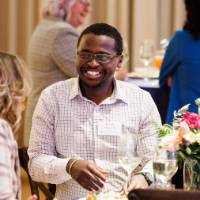 Three alum smile while chatting at a table